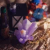Purple Crystal Spiritual Still Life | Meriem Chrrouhi Lavender crystal-shaped ornament with a gold pendant, lantern and bottles on warm fabric.
