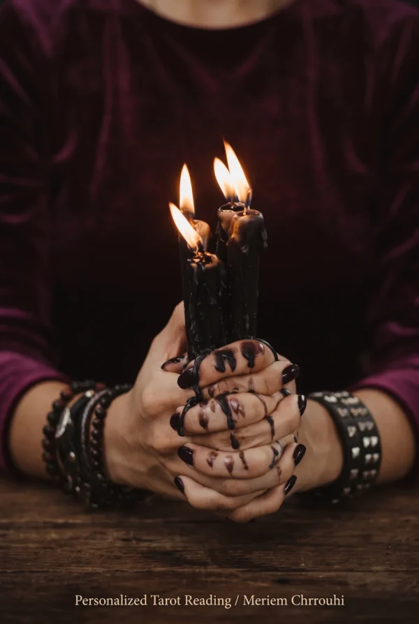 Hands holding black candles against a burgundy blouse, with the face outside the frame.
