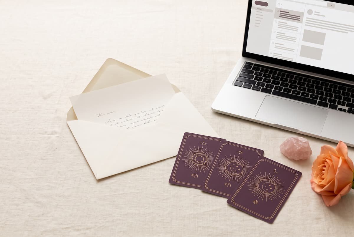 Laptop displaying an email beside an open envelope, purple tarot cards, rose quartz and a peach rose