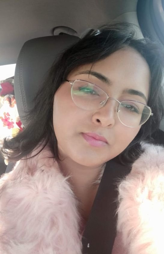 Meriem Chrrouhi wearing glasses and a soft pink collar, seated in a car.