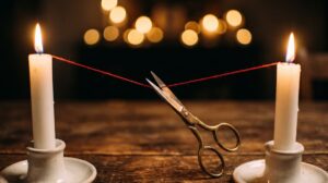 Cord cutting ritual: brass scissors cutting a red thread between two lit candles, a release ritual by PuraTarot
