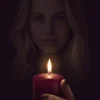 Red candle in the foreground with a softly shadowed blonde woman behind it.