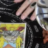 The Lovers tarot card beside a crystal ball and a ringed hand on a black zodiac cloth.